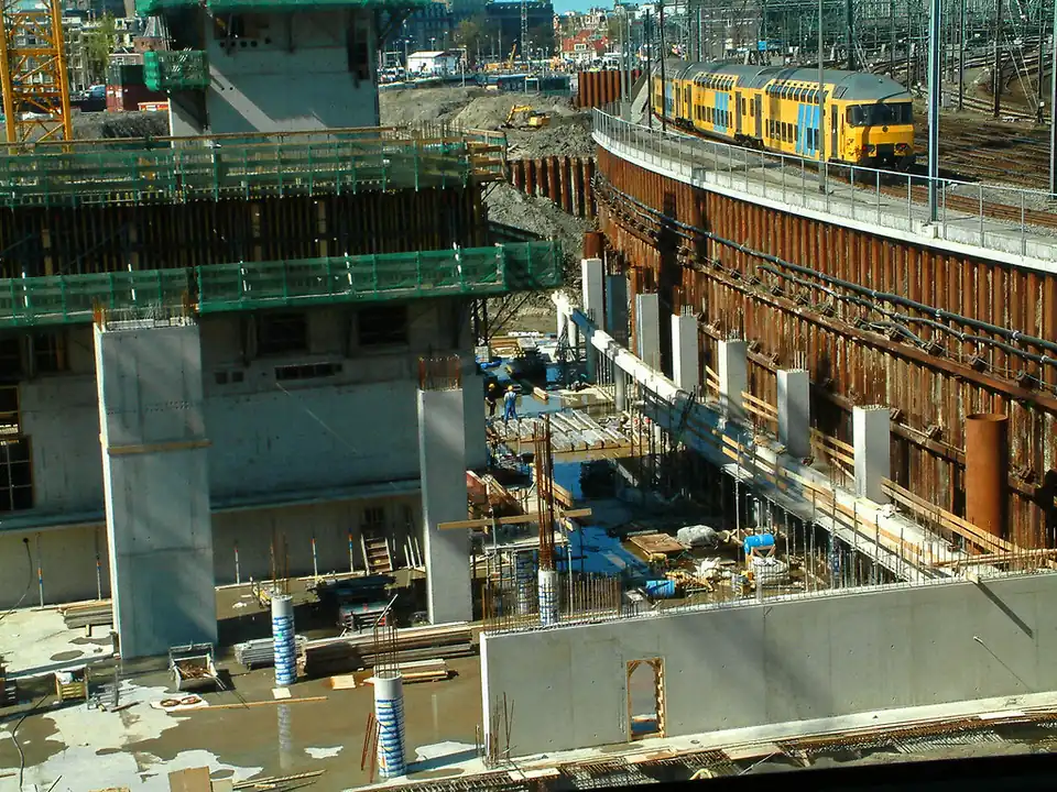 Excavación profunda con muros de contención y columnas de cimentación junto a una vía de tren